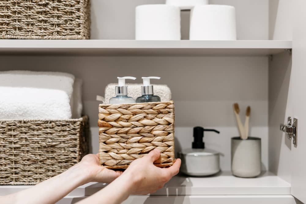 Mujer pone caja de mimbre con productos cosméticos en armario de baño
